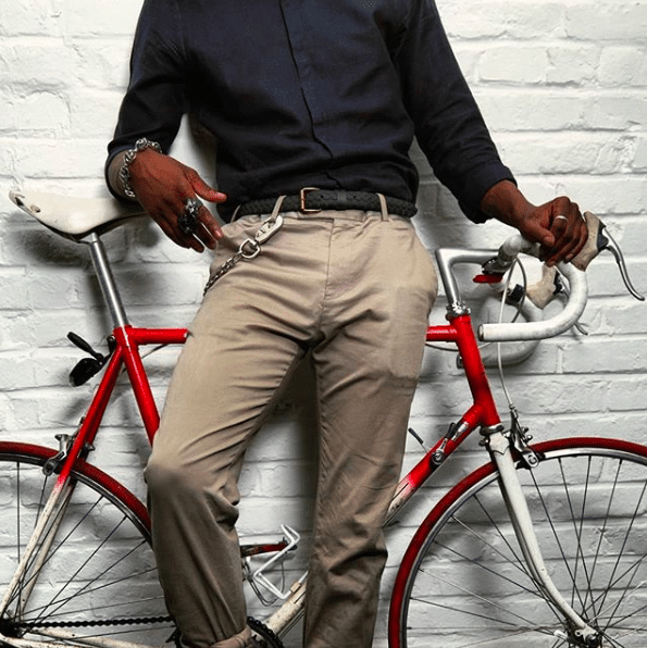 Un homme adossé sur un vélo portant une ceinture de la marque la vie est Belt